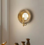 Lit Clérachic candle-style wall light with a round wood surround, on a pale wall above small stoneware pots.