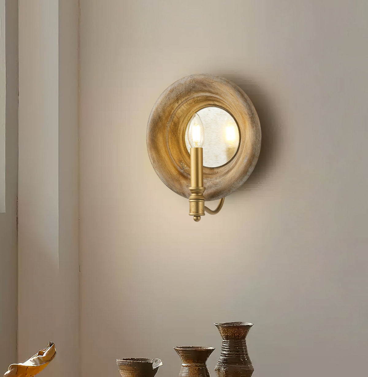 Lit Clérachic candle-style wall light with a round wood surround, on a pale wall above small stoneware pots.