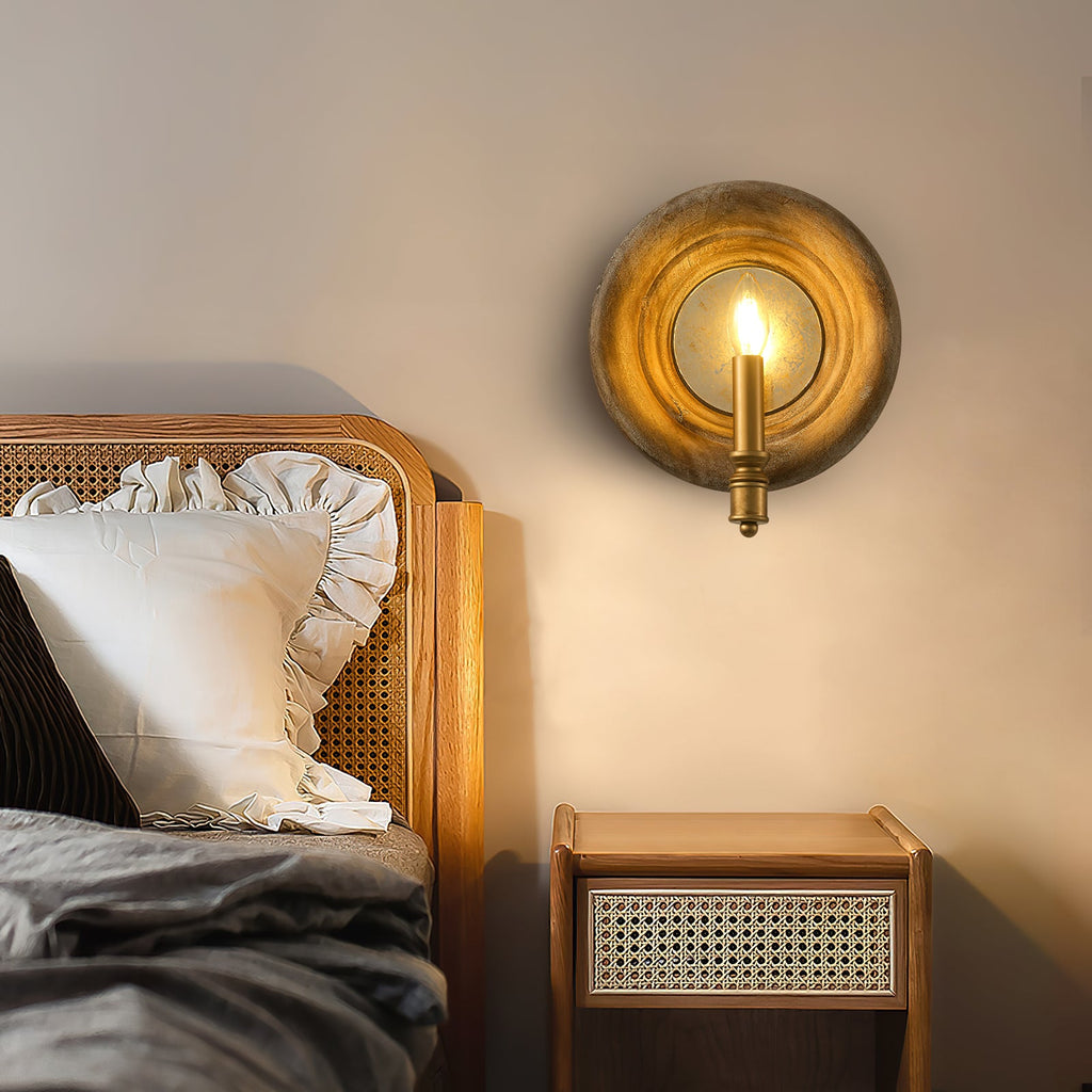 Clérachic round wood wall light with a lit candle bulb, above a rattan-backed bed and a rattan-fronted bedside table.