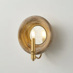 Angled view of a Clérachic wall light with a round wood surround, a mirrored disc and a gold candle-style arm, on a pale wall.