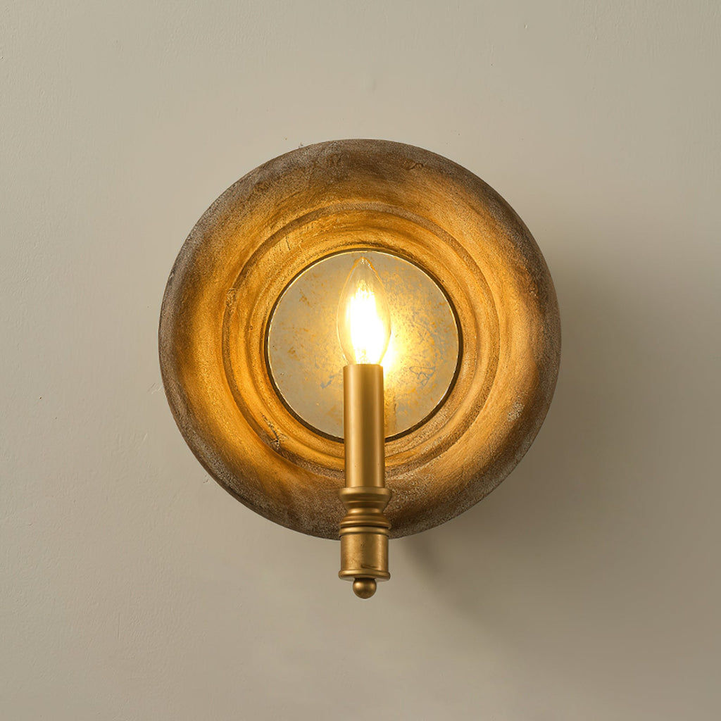 Front view of a Clérachic round wood wall light glowing warmly around its candle bulb, on a taupe wall.