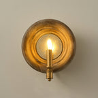 Front view of a Clérachic round wood wall light glowing warmly around its candle bulb, on a taupe wall.
