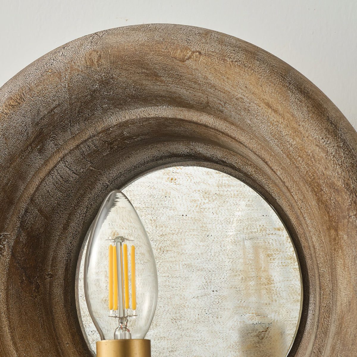 Close view of the wood surround, the aged mirror disc and a filament candle bulb on this Clérachic wall light.