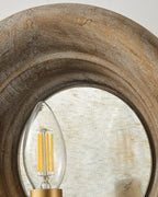 Close view of the rim of weathered wood and a candle bulb in front of the mirror on this Clérachic wall light.