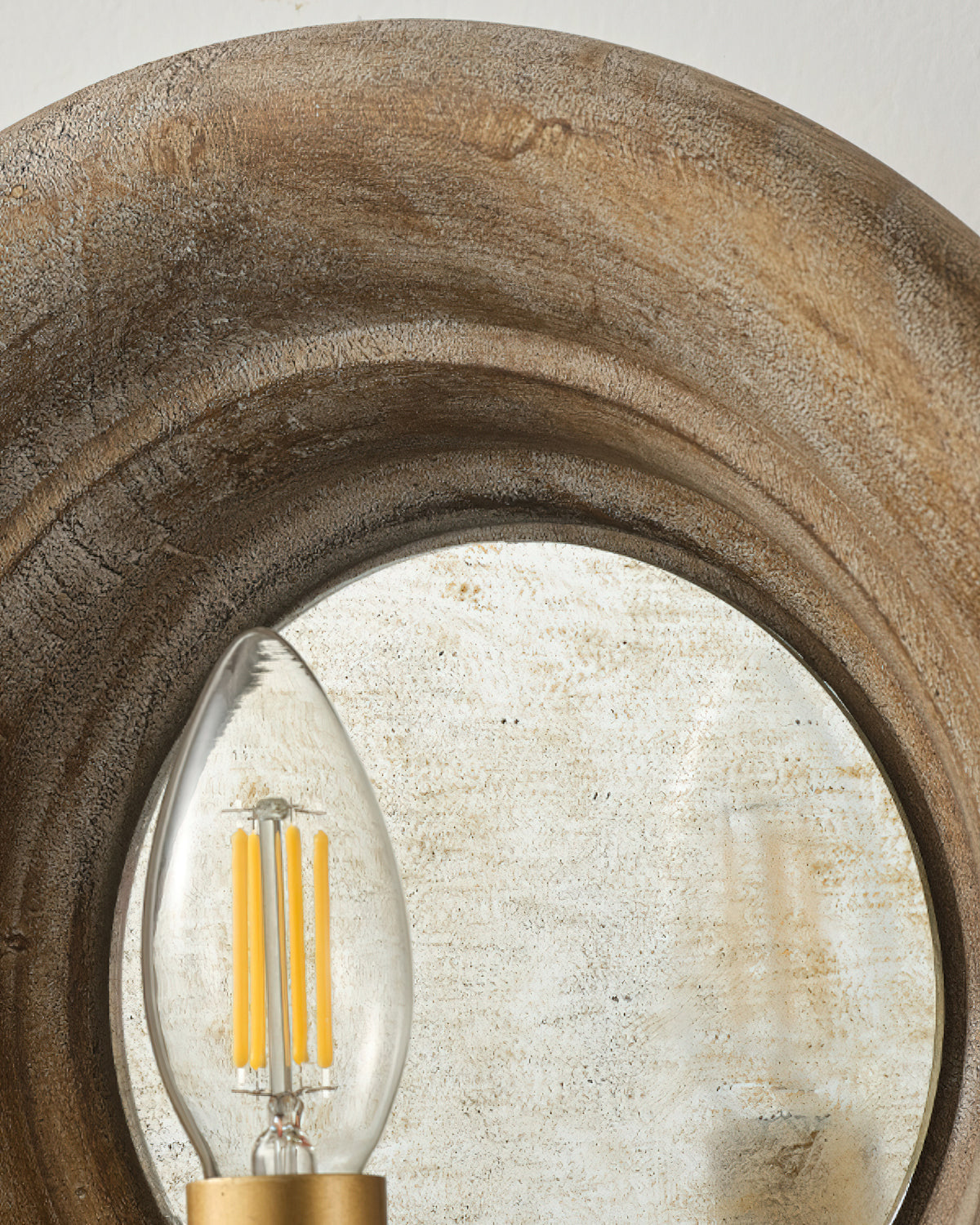 Close view of the rim of weathered wood and a candle bulb in front of the mirror on this Clérachic wall light.
