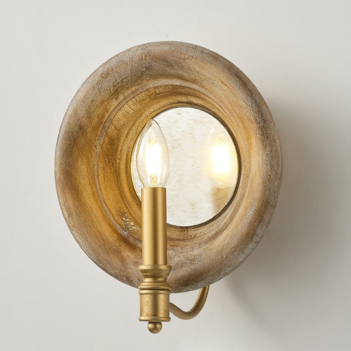 Clérachic wall light with a round wood surround, a mirror disc and a gold candle fitting, on a pale grey wall.