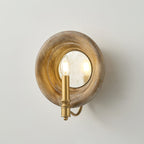 A smaller view of the Clérachic round wood wall light with its gold candle fitting and curved arm, on a pale grey wall.