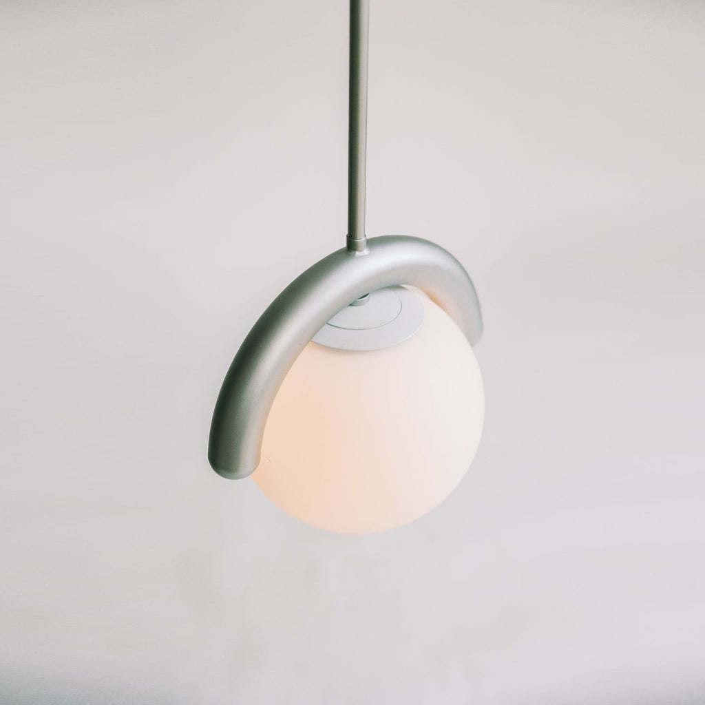 The Clérachic Citheis pendant lit from below, its hooked arm curling over the glass globe.