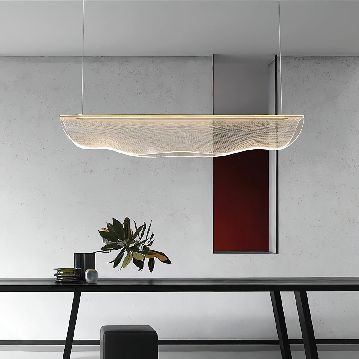 Above a black dining table with a plant and a dark stool, this Clérachic pendant light floats in front of a pale grey wall.