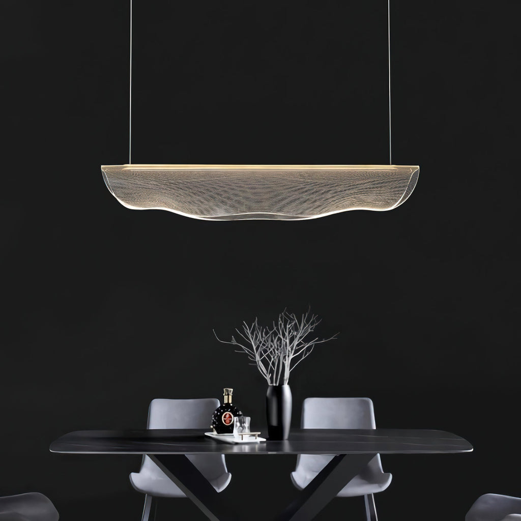 Lit against a near-black wall, this Clérachic pendant light hangs above a dark table with grey chairs and a bare branch in a vase.