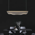 Lit against a near-black wall, this Clérachic pendant light hangs above a dark table with grey chairs and a bare branch in a vase.