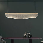 In a dark green-grey room, this Clérachic pendant light hangs above a dark oval table with small ceramic pieces.