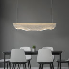 A Clérachic pendant light over a black table with pale grey chairs and a small plant, in front of a grey wall.