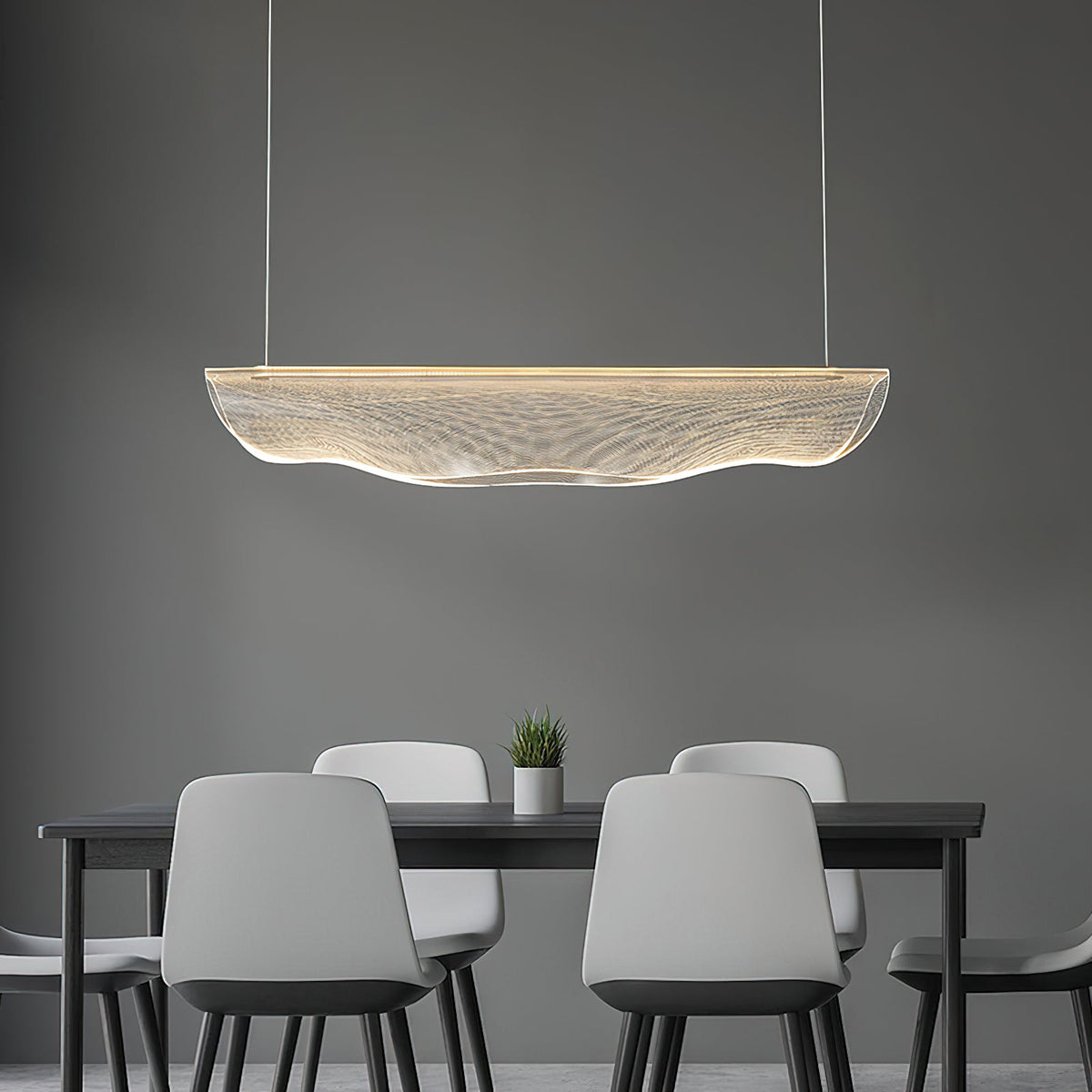 A Clérachic pendant light over a black table with pale grey chairs and a small plant, in front of a grey wall.