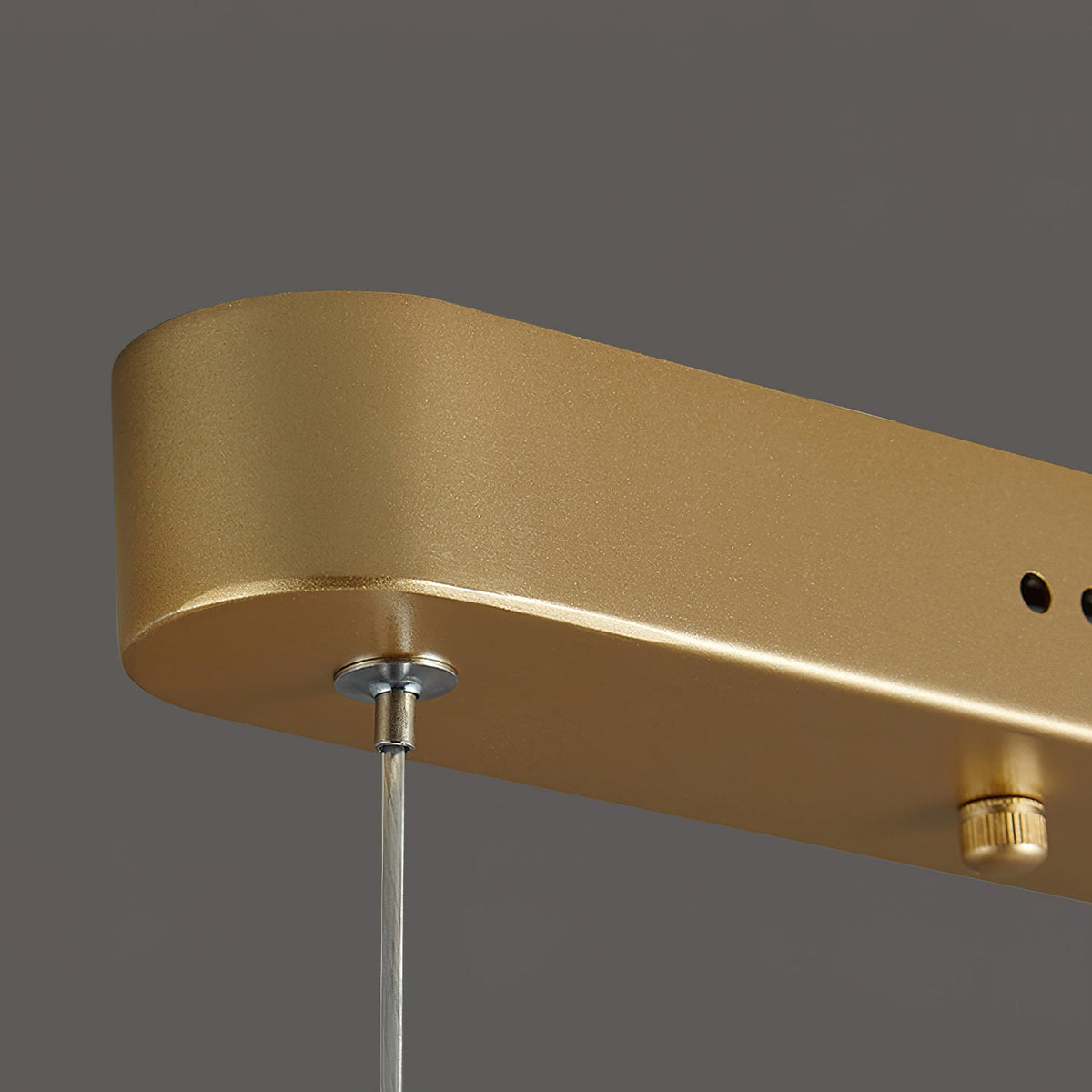 Close view of the gold canopy end on this Clérachic pendant light, with a clear wire gripper and a small adjusting knob.