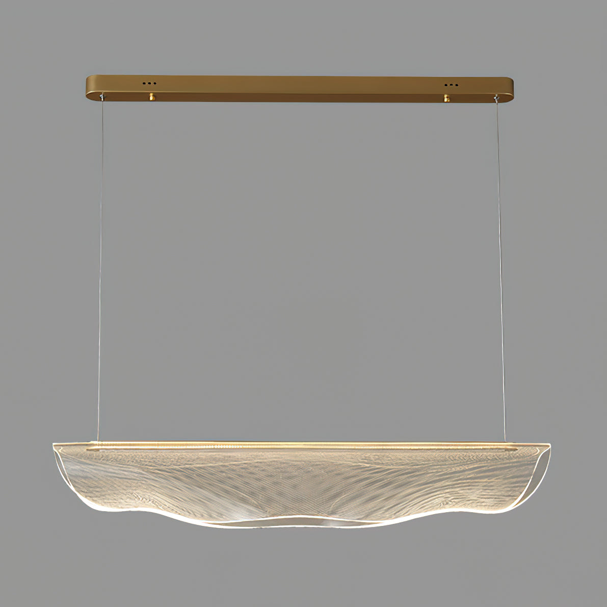 Close view of the unlit clear shade on this Clérachic pendant light, wavy at the lower edge, with gold canopy and wires above.