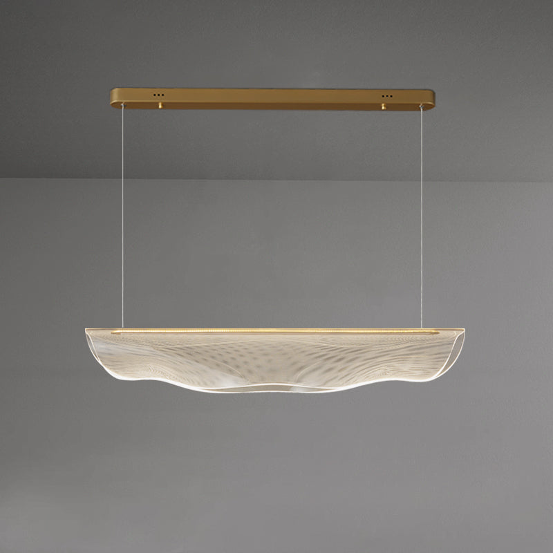 This Clérachic pendant light lit on a grey backdrop, its gold canopy bar high above the glowing, rippled shade.