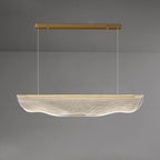 Wide view of this Clérachic pendant light lit against a grey wall, its long clear shade hung well below the gold canopy.