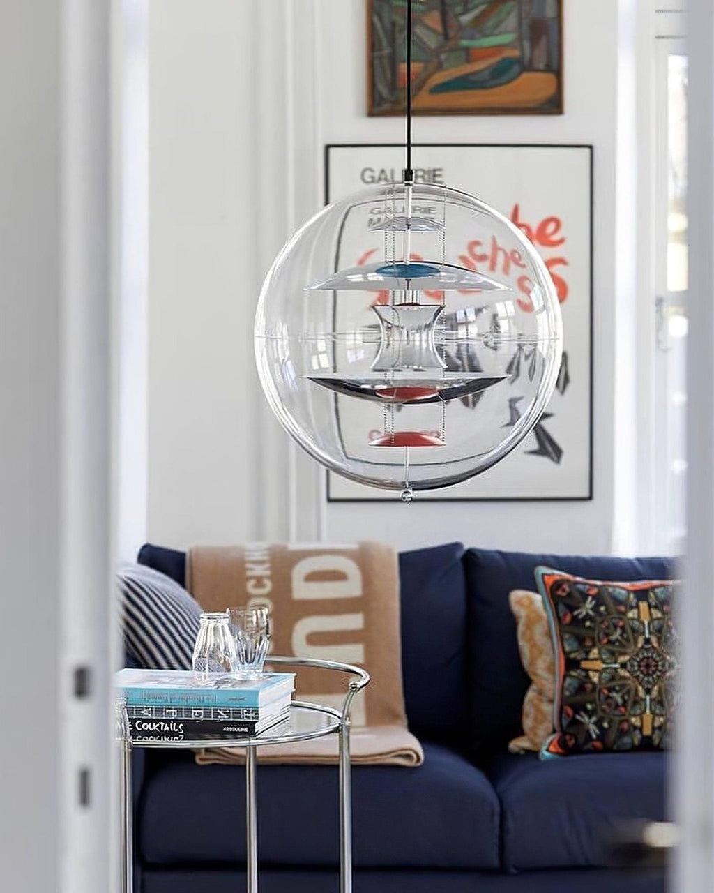 This Clérachic sphere pendant hangs in a living-room doorway above a navy sofa, with a framed poster on the wall behind it.