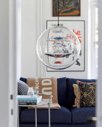 This Clérachic sphere pendant hangs in a living-room doorway above a navy sofa, with a framed poster on the wall behind it.