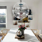 Close to the camera, a Clérachic clear sphere pendant hangs over a white dining table set with pink roses and wishbone-style chairs.
