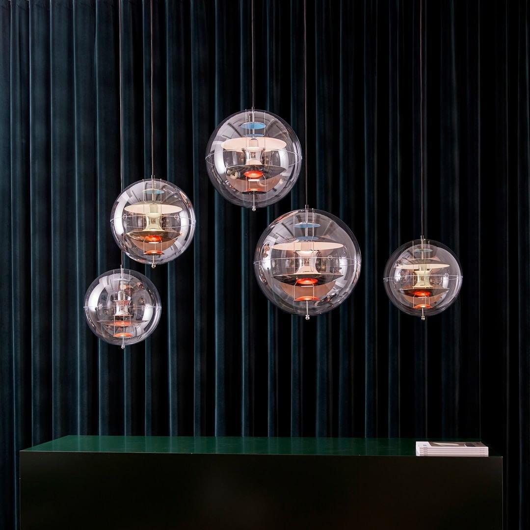 A cluster of five Clérachic sphere pendants hangs at different heights against dark green curtains, glowing warm from inside.