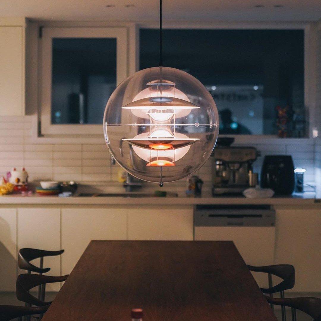 Lit in the evening, this Clérachic sphere pendant casts a soft glow over a dark wood dining table with a kitchen behind it.