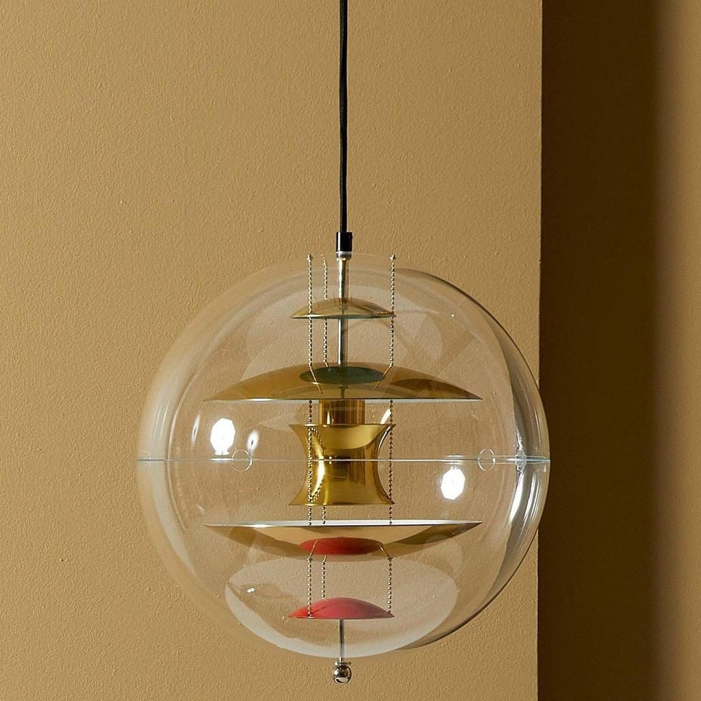 Hung against a warm ochre wall, this Clérachic sphere pendant shows brass-toned discs and red dishes inside its clear acrylic globe.