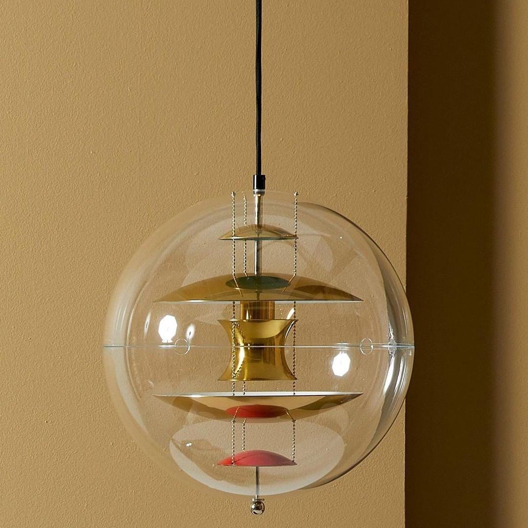 Hung against a warm ochre wall, this Clérachic sphere pendant shows brass-toned discs and red dishes inside its clear acrylic globe.