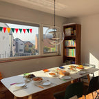A Clérachic sphere pendant hangs by a sunny window over a white table laid with bowls and plates, with a bookcase to one side.