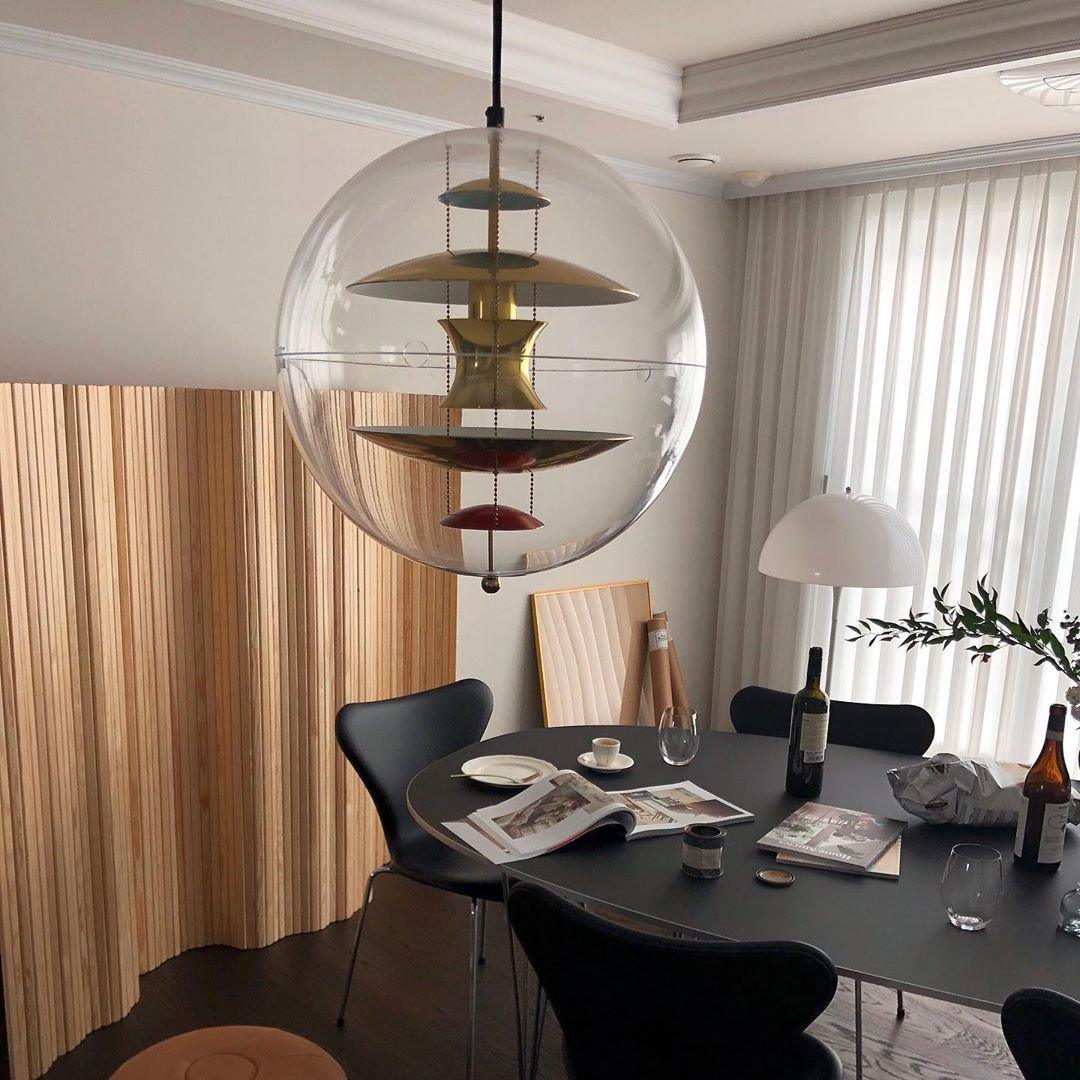 This Clérachic sphere pendant with gold-toned discs hangs in a dining room with a dark table, black chairs and long curtains.