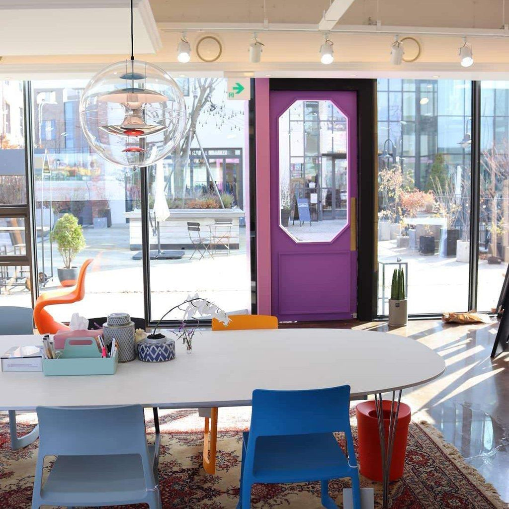 A Clérachic sphere pendant hangs high in a bright studio with a large window, track lights and a long white oval table below.