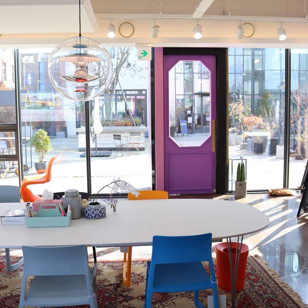 A Clérachic sphere pendant hangs high in a bright studio with a large window, track lights and a long white oval table below.