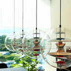 Four Clérachic sphere pendants of rising size hang in a row against a bright window, their metal discs reflecting the daylight.