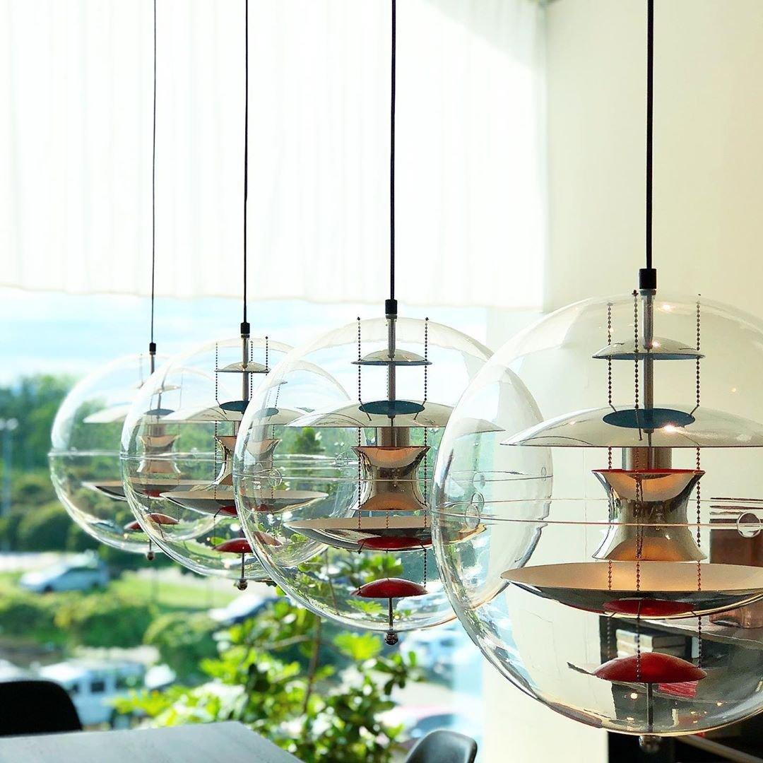 Four Clérachic sphere pendants of rising size hang in a row against a bright window, their metal discs reflecting the daylight.