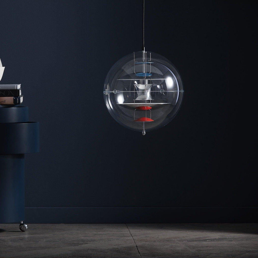 Against a deep navy wall, this Clérachic sphere pendant hangs on a thin cord, its white discs and red dish visible through the clear acrylic.