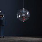 Against a deep navy wall, this Clérachic sphere pendant hangs on a thin cord, its white discs and red dish visible through the clear acrylic.