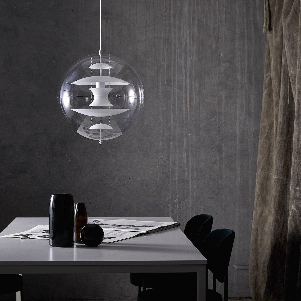 This Clérachic sphere pendant with white discs hangs against a concrete-grey wall above a table with dark vases and papers.