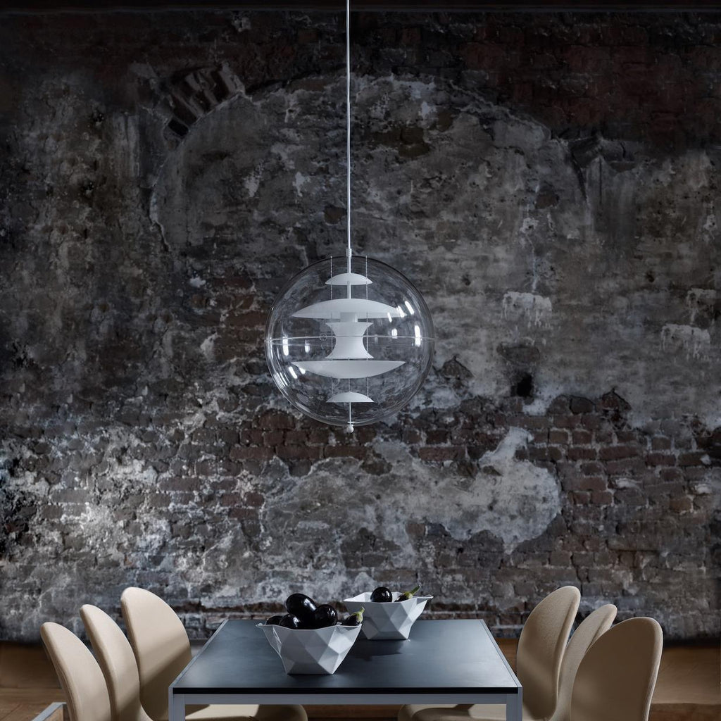 A small Clérachic sphere pendant hangs in front of a weathered dark brick wall, with chairs and a black table beneath it.