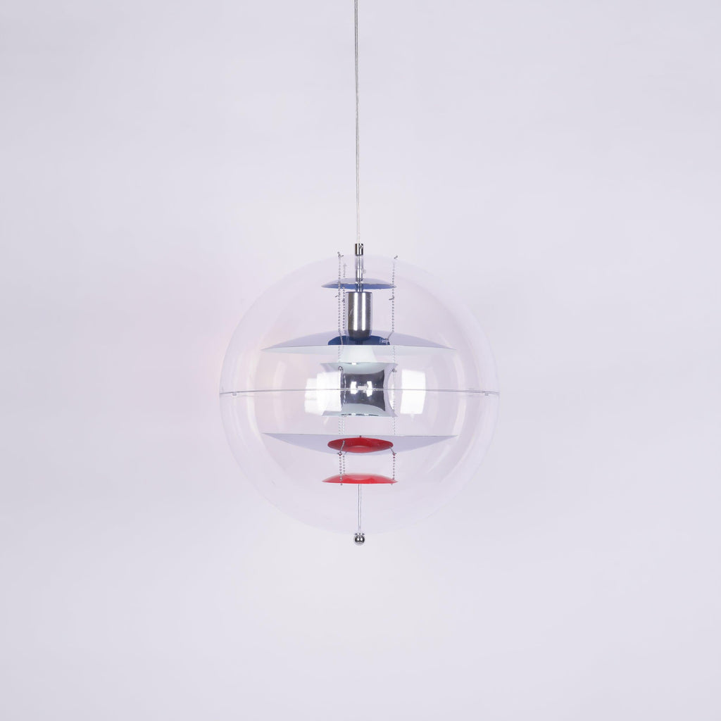 Product photo of a Clérachic sphere pendant on a pale lilac backdrop, with chrome discs and red dishes inside the clear globe.