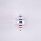 Product photo of a Clérachic sphere pendant on a pale lilac backdrop, with chrome discs and red dishes inside the clear globe.