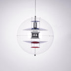 This Clérachic sphere pendant hangs on a clear cord against a soft grey-lilac backdrop, with a red dish at the base of the stack.