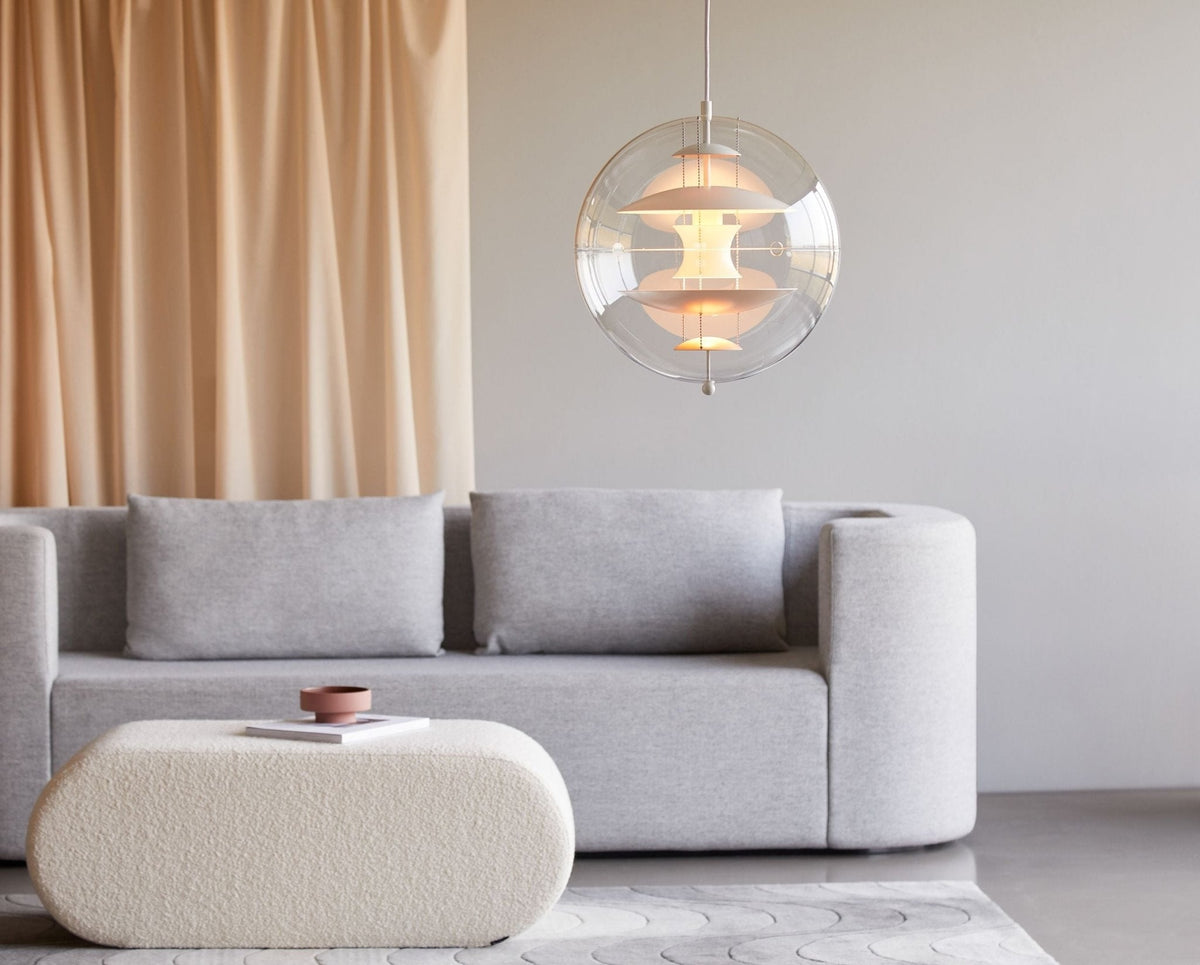 Lit softly, this Clérachic sphere pendant hangs beside peach curtains above a grey sofa and a rounded cream ottoman.