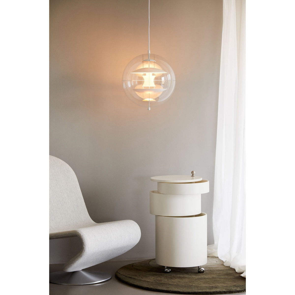 Glowing warm and white, this Clérachic sphere pendant hangs by sheer curtains next to a white armchair and a cylindrical side table.