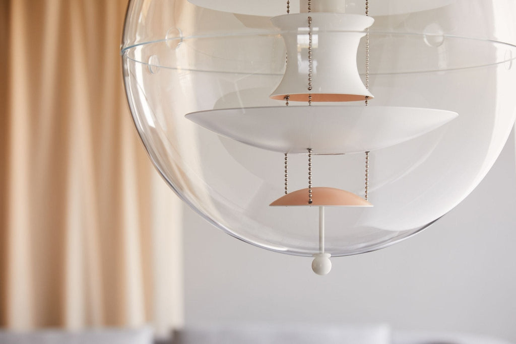 Close view of the white discs and apricot dish inside this Clérachic sphere pendant, with warm curtains softly blurred behind.
