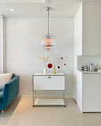 A small Clérachic sphere pendant hangs in a white room above a white cabinet, beside a teal sofa and a red mobile.