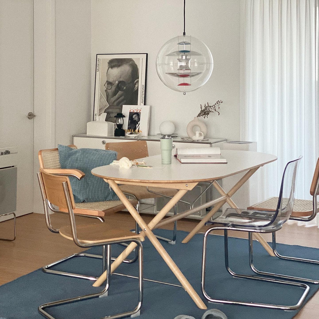This Clérachic sphere pendant hangs over an oval table with cane chairs and clear chairs, a framed portrait behind it, on a blue rug.