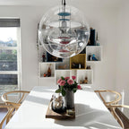 From a low angle, this Clérachic sphere pendant hangs above a white table with pink roses, in front of a window and cube shelves.
