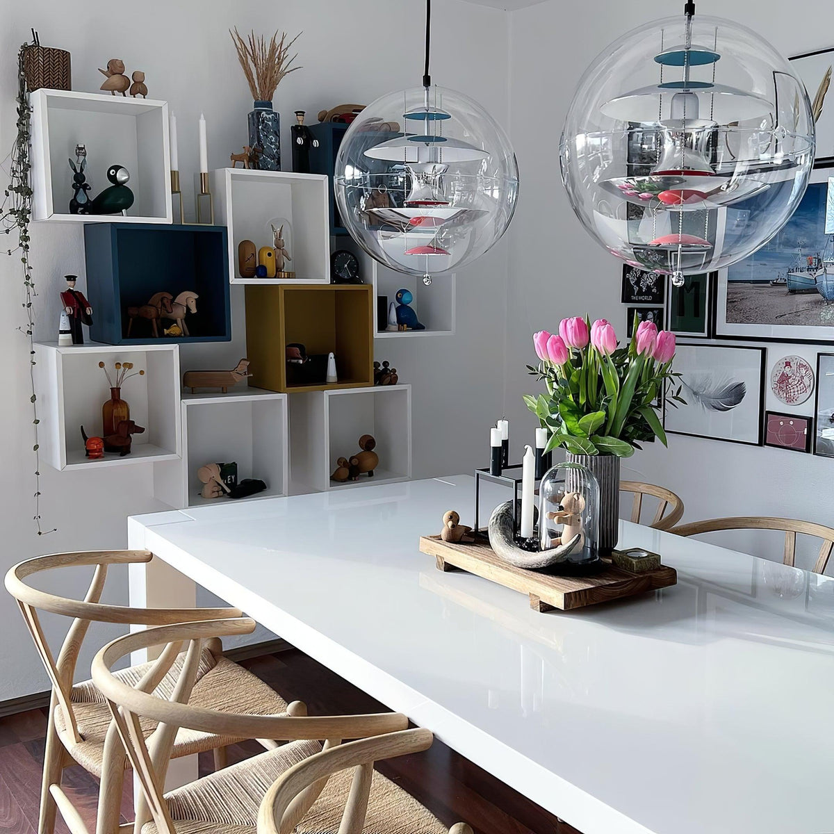 Two Clérachic sphere pendants hang above a glossy white table with a tulip bouquet, beside cube shelves holding small ornaments.