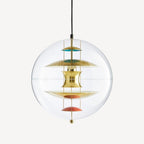 A Clérachic sphere pendant in gold on an off-white backdrop, with brass discs and coral dishes hanging on chains inside the clear sphere.